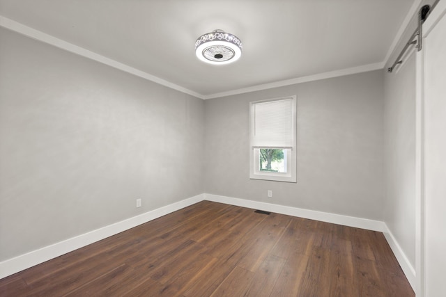 empty room with a barn door, crown molding, and hardwood / wood-style flooring