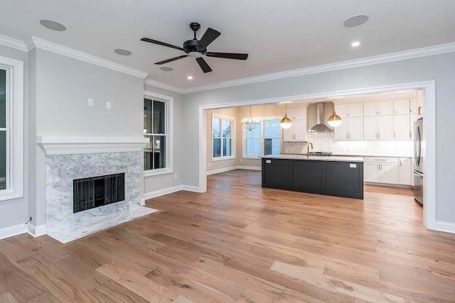 kitchen with an island with sink, backsplash, light hardwood / wood-style flooring, wall chimney range hood, and decorative light fixtures