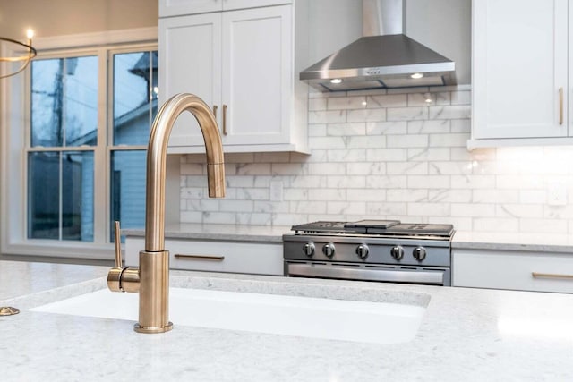 kitchen with white cabinets, high end stainless steel range oven, light stone countertops, and wall chimney range hood