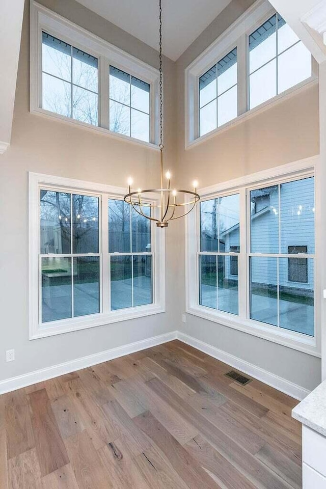 unfurnished dining area with a notable chandelier, a towering ceiling, and wood-type flooring