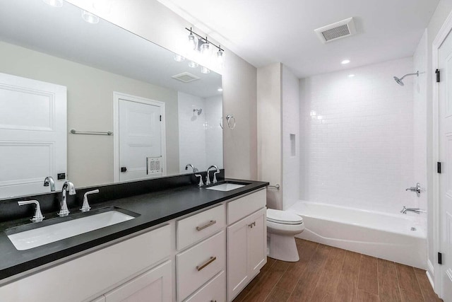 full bathroom with double vanity, toilet, tiled shower / bath combo, and wood-type flooring