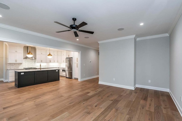 kitchen featuring hanging light fixtures, appliances with stainless steel finishes, an island with sink, light hardwood / wood-style floors, and wall chimney range hood