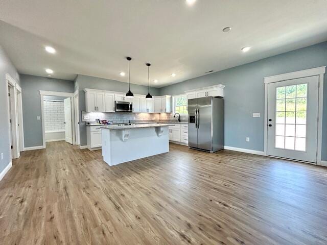 kitchen with appliances with stainless steel finishes, white cabinets, backsplash, and wood finished floors