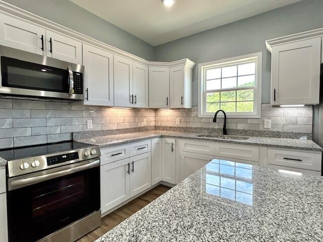 kitchen with appliances with stainless steel finishes, dark hardwood / wood-style floors, tasteful backsplash, sink, and white cabinets