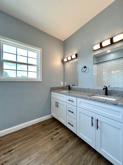 full bath with double vanity, wood finished floors, a sink, and baseboards