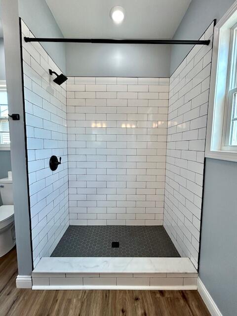 full bath featuring toilet, wood finished floors, and tiled shower