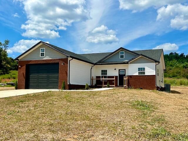 view of front of home with central AC unit, an attached garage, brick siding, driveway, and a front lawn