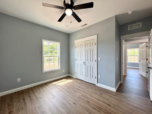 unfurnished bedroom with a closet, ceiling fan, multiple windows, and hardwood / wood-style flooring