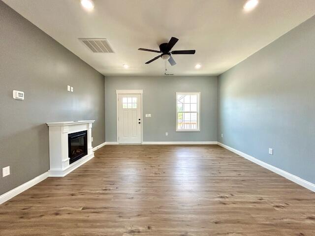 unfurnished living room featuring wood finished floors, a glass covered fireplace, visible vents, and baseboards