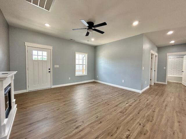 unfurnished living room featuring a fireplace, wood finished floors, a ceiling fan, and baseboards