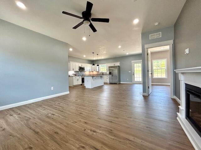 unfurnished living room featuring dark wood-style floors, recessed lighting, a ceiling fan, a glass covered fireplace, and baseboards