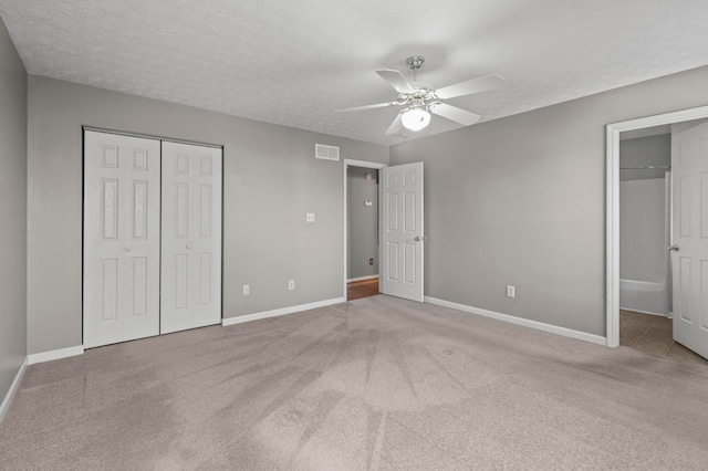 unfurnished bedroom featuring a textured ceiling, connected bathroom, carpet flooring, and ceiling fan