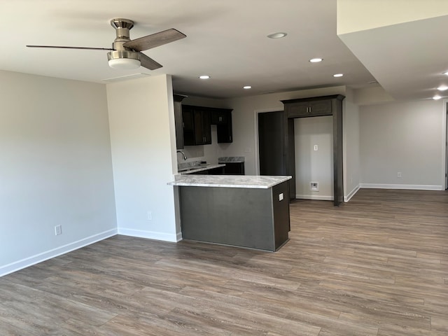 kitchen with light stone countertops, kitchen peninsula, wood-type flooring, and ceiling fan