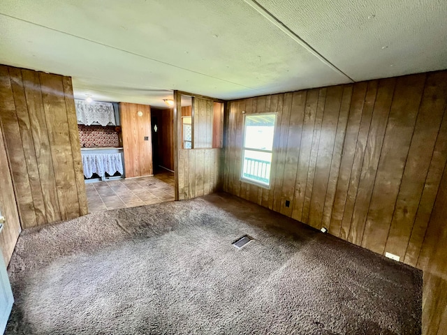 carpeted empty room featuring wooden walls and a textured ceiling