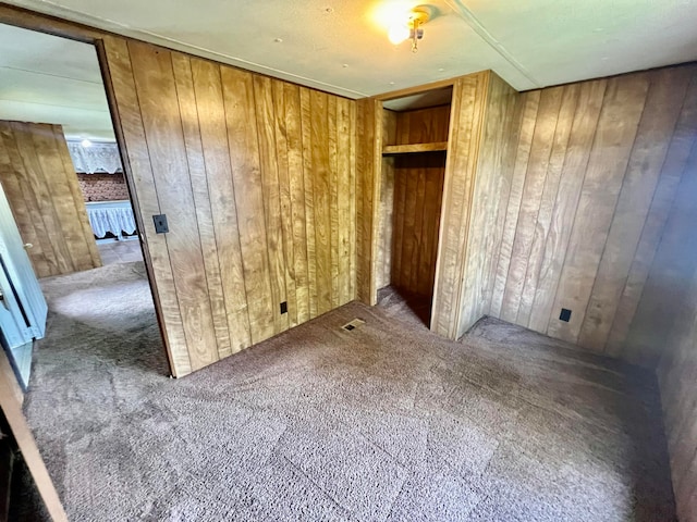 unfurnished bedroom featuring wood walls, carpet flooring, and a closet