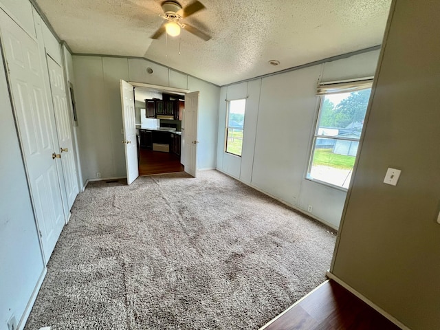 unfurnished bedroom with lofted ceiling, a textured ceiling, light colored carpet, and ceiling fan