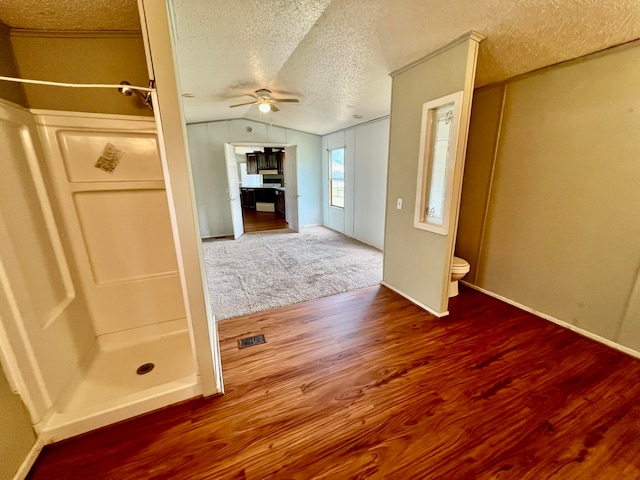 interior space with ceiling fan, a textured ceiling, lofted ceiling, and toilet