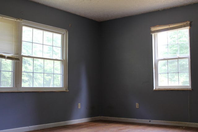 spare room with a wealth of natural light, a textured ceiling, and hardwood / wood-style floors