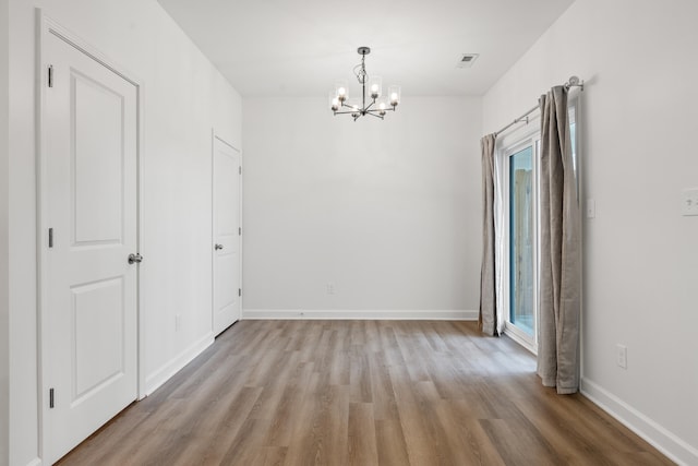 spare room with plenty of natural light, an inviting chandelier, and light hardwood / wood-style flooring