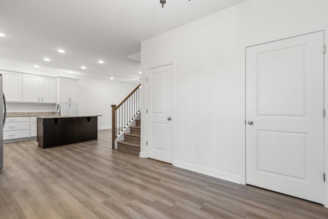 kitchen with white cabinets, a kitchen breakfast bar, a center island with sink, stainless steel fridge, and light wood-type flooring