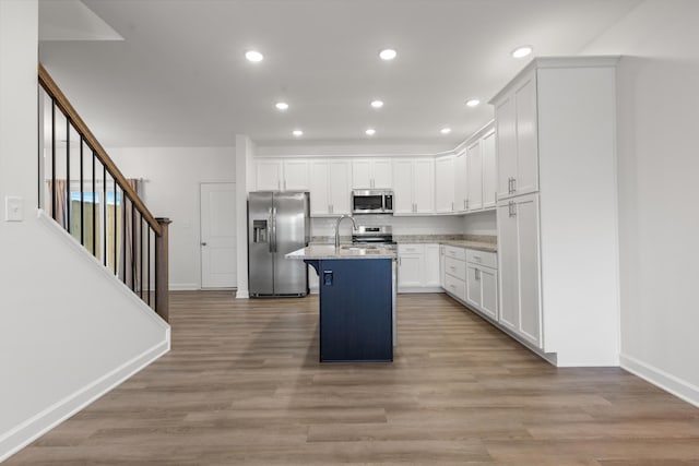 kitchen featuring light stone countertops, a breakfast bar area, a kitchen island with sink, white cabinets, and appliances with stainless steel finishes