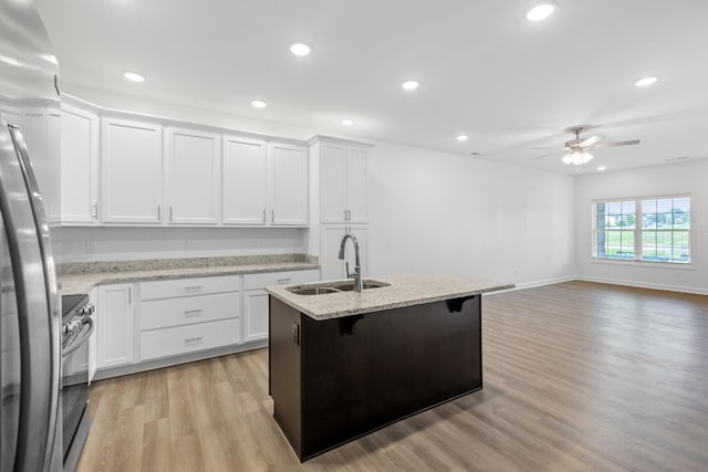 kitchen with a kitchen bar, a kitchen island with sink, sink, light hardwood / wood-style floors, and white cabinetry