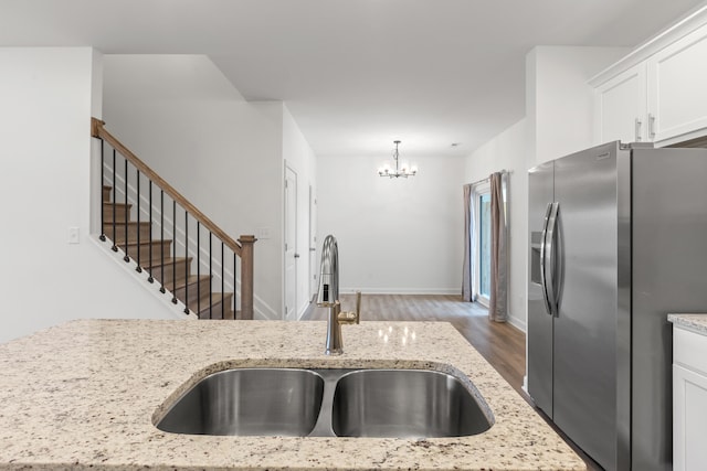 kitchen with light stone counters, dark wood-type flooring, sink, pendant lighting, and stainless steel fridge with ice dispenser