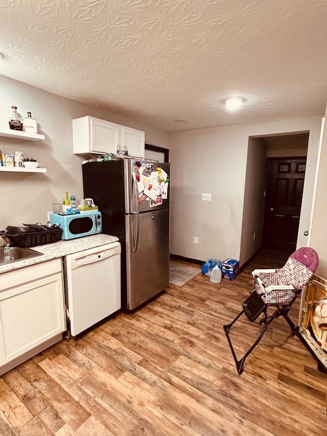 kitchen featuring white cabinets, white appliances, a textured ceiling, and light wood-type flooring