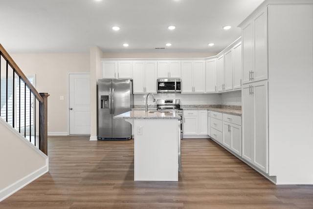 kitchen featuring an island with sink, white cabinetry, stainless steel appliances, and light stone counters