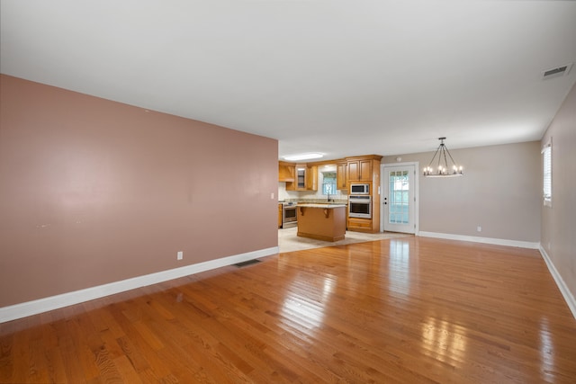 unfurnished living room with sink, a notable chandelier, and light wood-type flooring