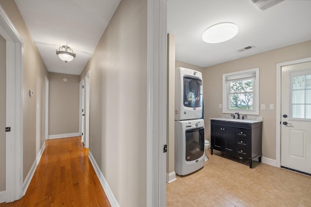 hallway featuring stacked washer and dryer, light wood-type flooring, and sink