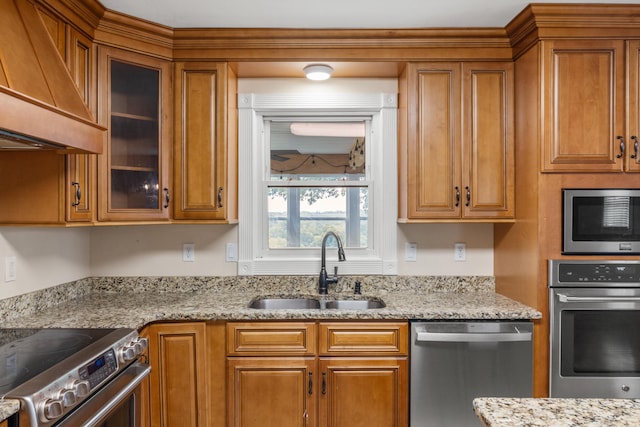 kitchen featuring appliances with stainless steel finishes, sink, custom range hood, and light stone countertops