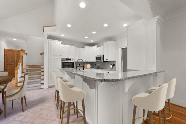 kitchen featuring decorative backsplash, white cabinets, appliances with stainless steel finishes, light stone countertops, and a breakfast bar area