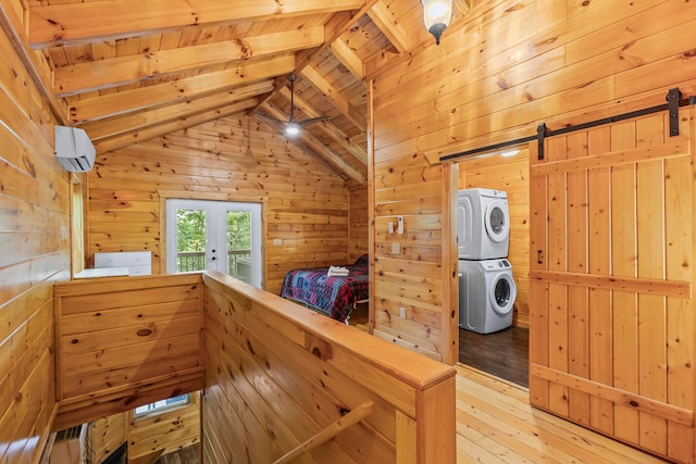 interior space with hardwood / wood-style floors, stacked washer and clothes dryer, a barn door, and wooden walls