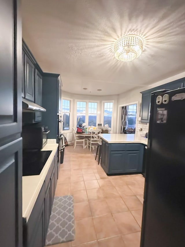 kitchen featuring black fridge, stovetop, tasteful backsplash, light tile patterned floors, and kitchen peninsula