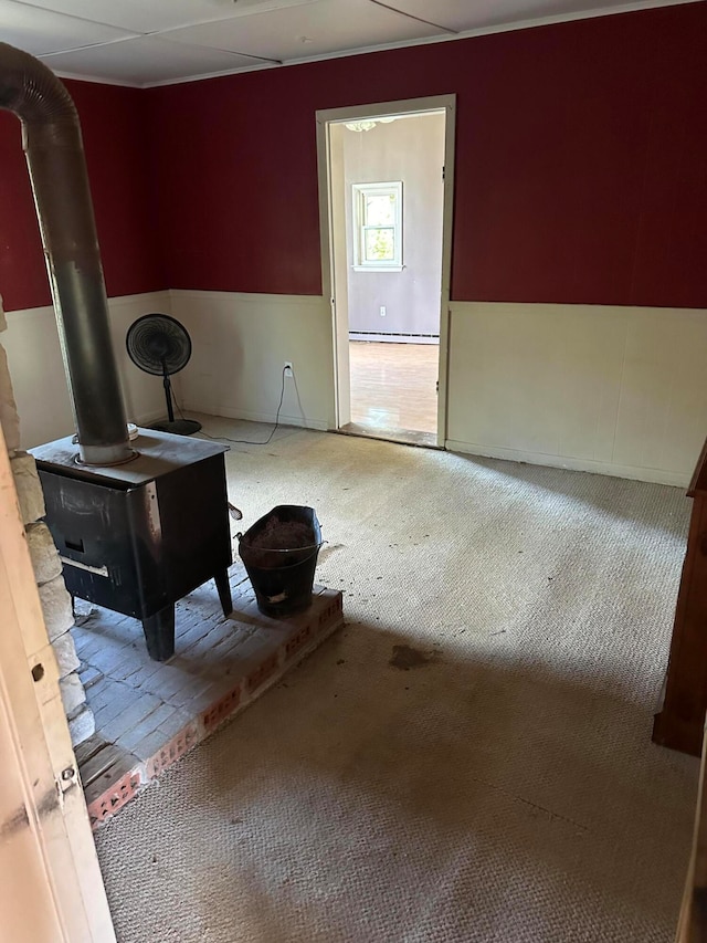 unfurnished living room featuring a baseboard radiator, a drop ceiling, carpet floors, and a wood stove