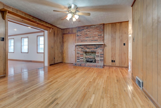 unfurnished living room with wooden walls, a brick fireplace, ceiling fan, a textured ceiling, and light hardwood / wood-style floors