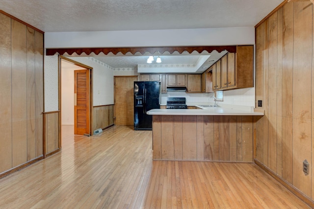 kitchen with sink, kitchen peninsula, wood walls, light hardwood / wood-style floors, and black appliances