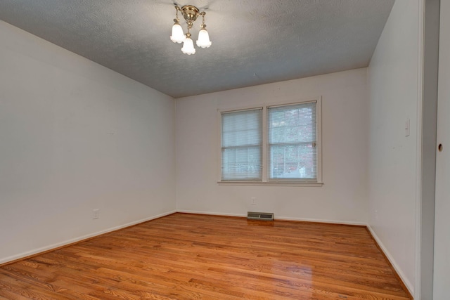 unfurnished room with a textured ceiling, light wood-type flooring, and a notable chandelier