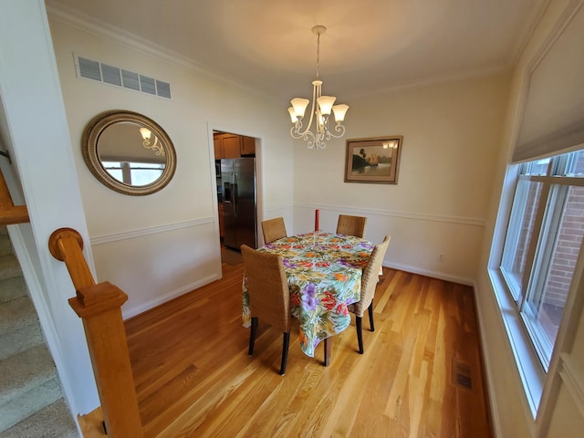 dining area with a notable chandelier, light wood-style flooring, visible vents, and crown molding