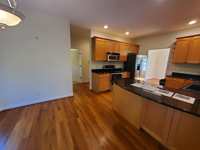 kitchen featuring stainless steel appliances, dark countertops, wood finished floors, and recessed lighting