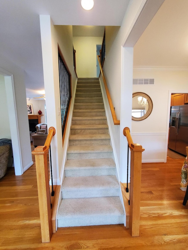 staircase with ornamental molding, wood finished floors, visible vents, and baseboards