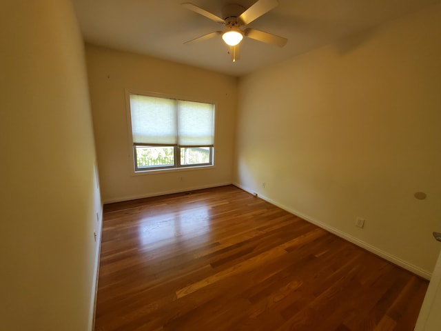 spare room with wood finished floors, a ceiling fan, and baseboards