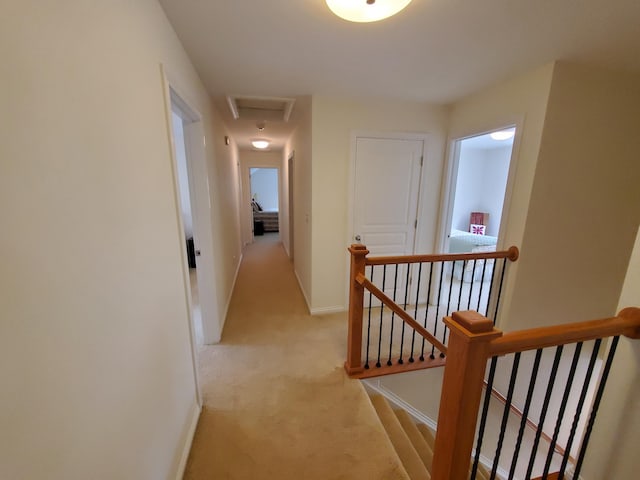 corridor with attic access, visible vents, baseboards, light colored carpet, and an upstairs landing