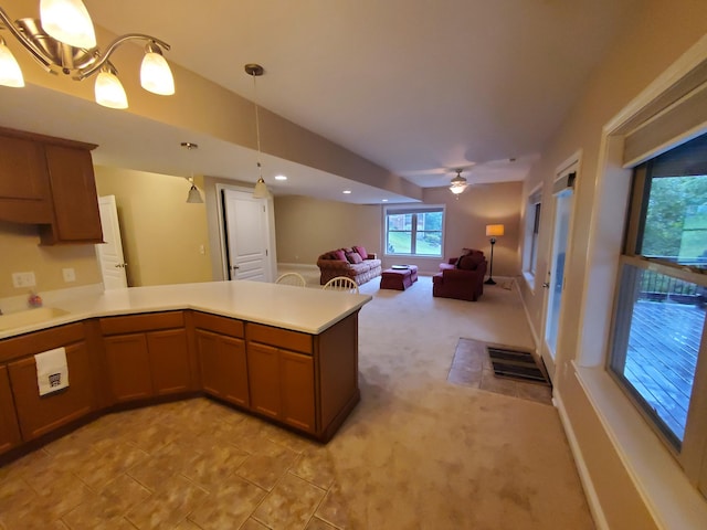 kitchen featuring light carpet, brown cabinetry, open floor plan, hanging light fixtures, and light countertops