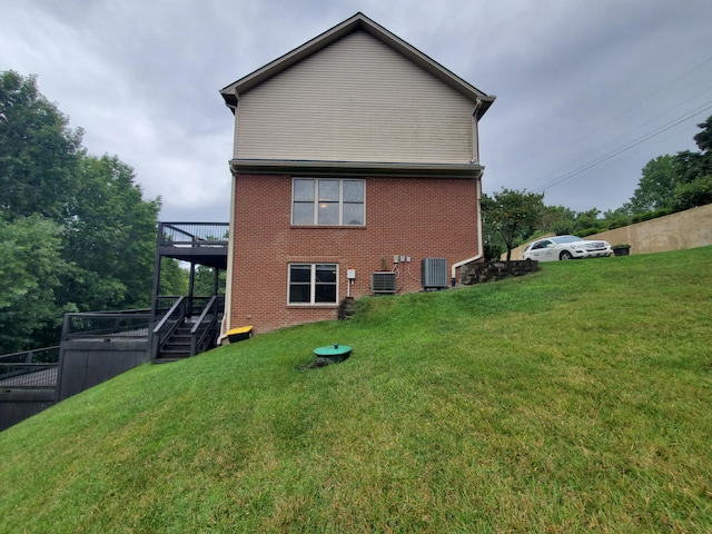 back of property featuring brick siding, a yard, a deck, and central air condition unit