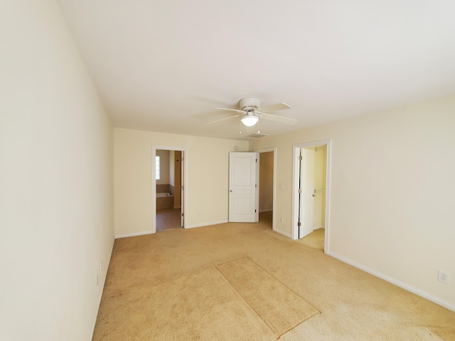 unfurnished bedroom featuring connected bathroom, light carpet, a ceiling fan, baseboards, and a walk in closet