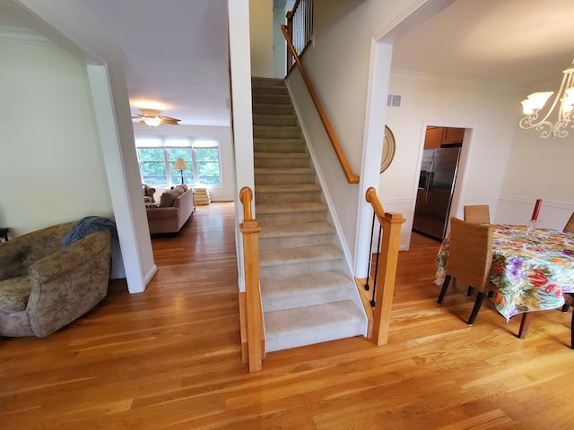 stairway featuring crown molding, visible vents, a notable chandelier, and wood finished floors