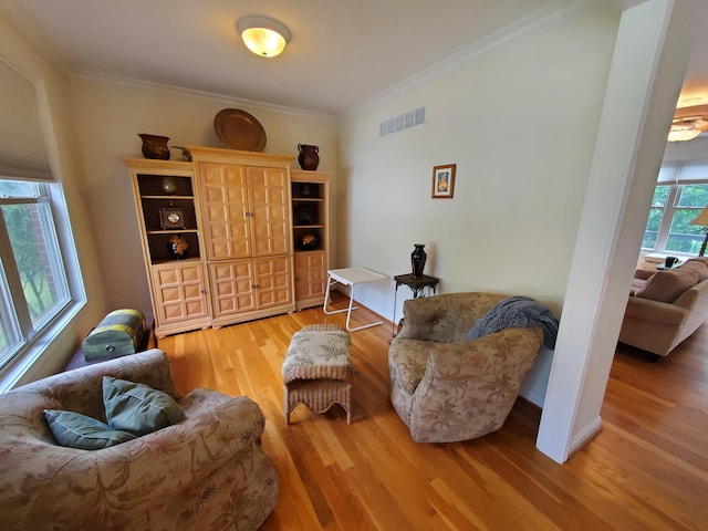 living area with ornamental molding, wood finished floors, visible vents, and baseboards