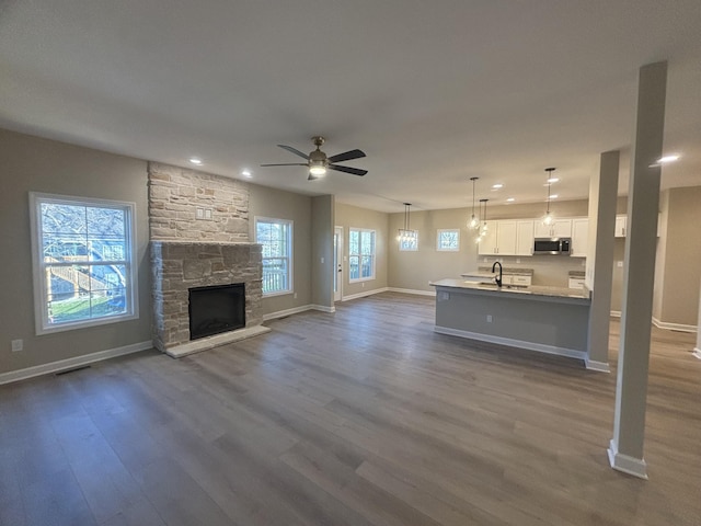 unfurnished living room featuring a fireplace, wood-type flooring, sink, and ceiling fan